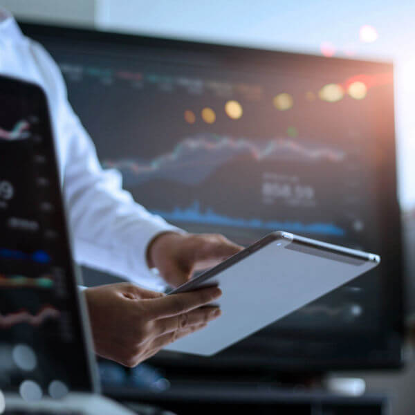 laptop with stock charts, man pointing to tablet, stock on computer monitor in background