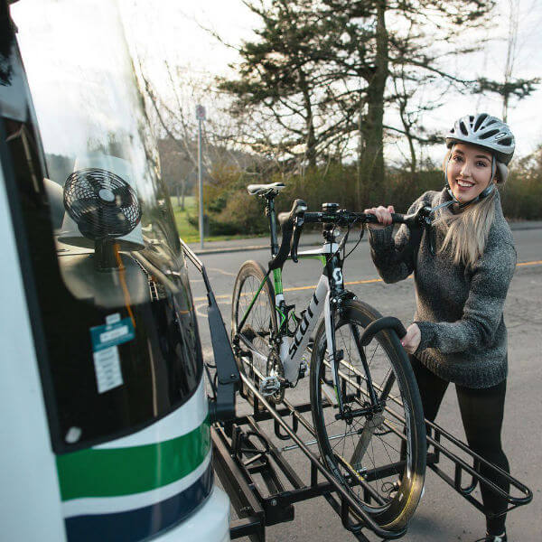 woman loads bicycle onto a bus bike rack
